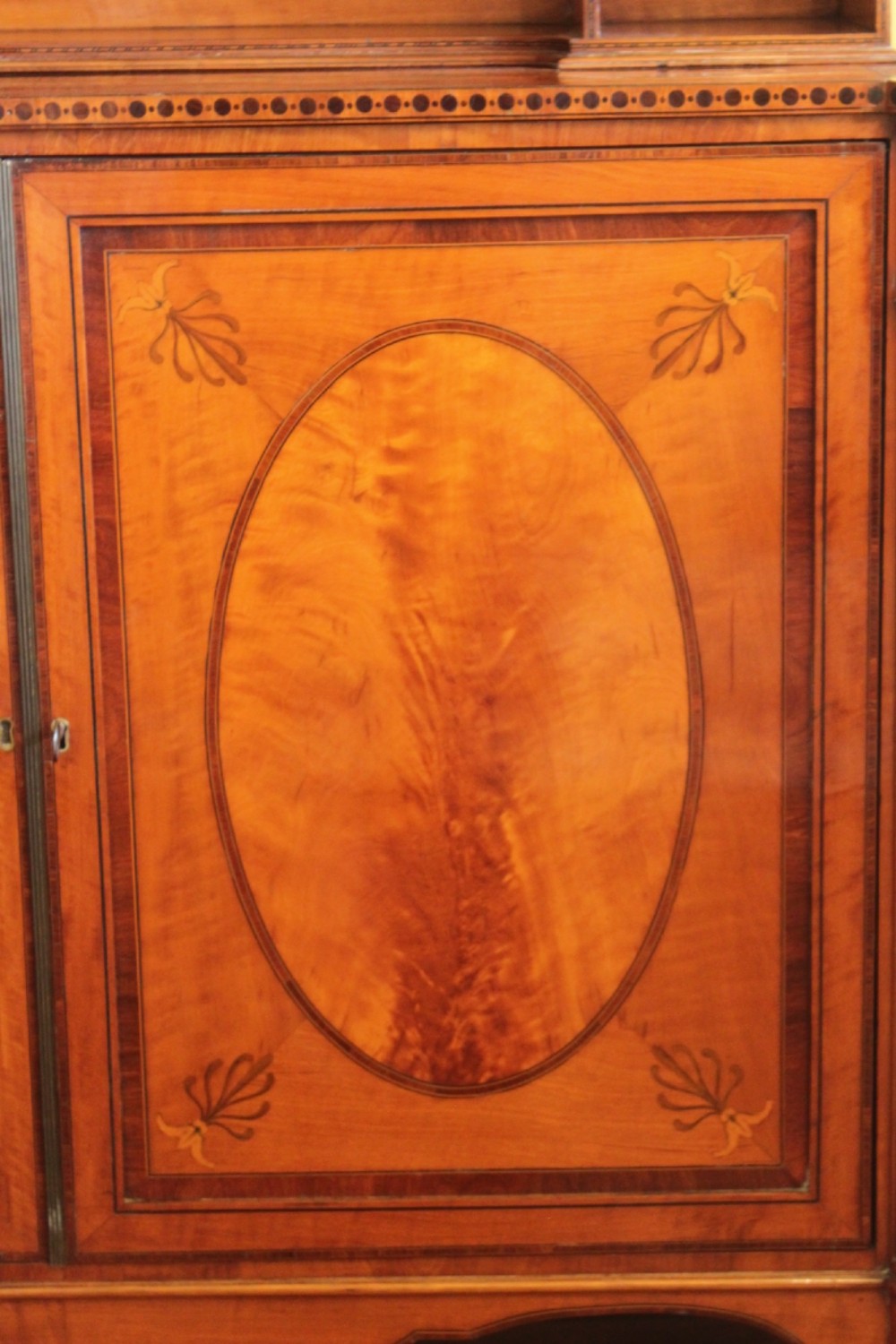 An antique Sheraton style satinwood cabinet with an open tiered shelving top unit and a lower two-door cabinet featuring oval inlaid marquetry panels. View III