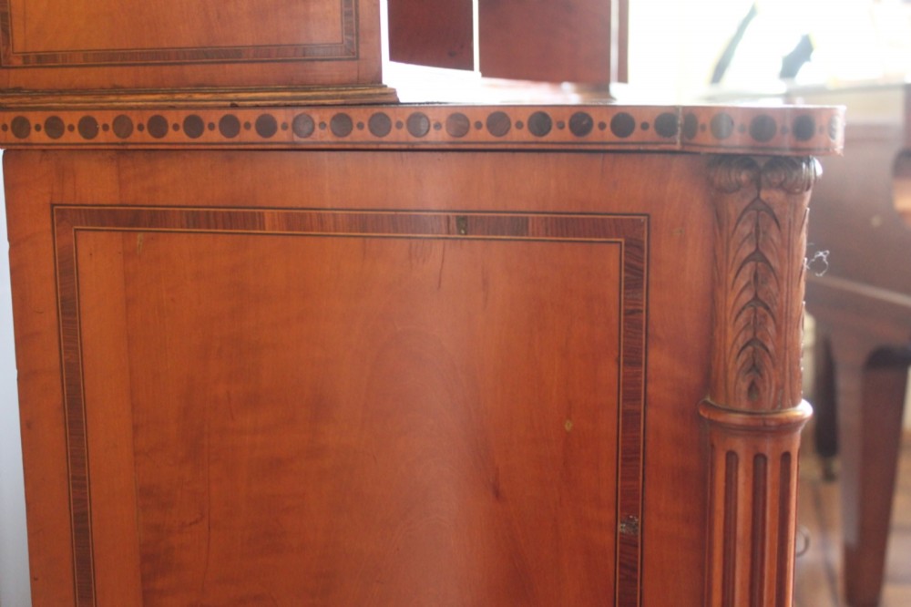 An antique Sheraton style satinwood cabinet with an open tiered shelving top unit and a lower two-door cabinet featuring oval inlaid marquetry panels. View X