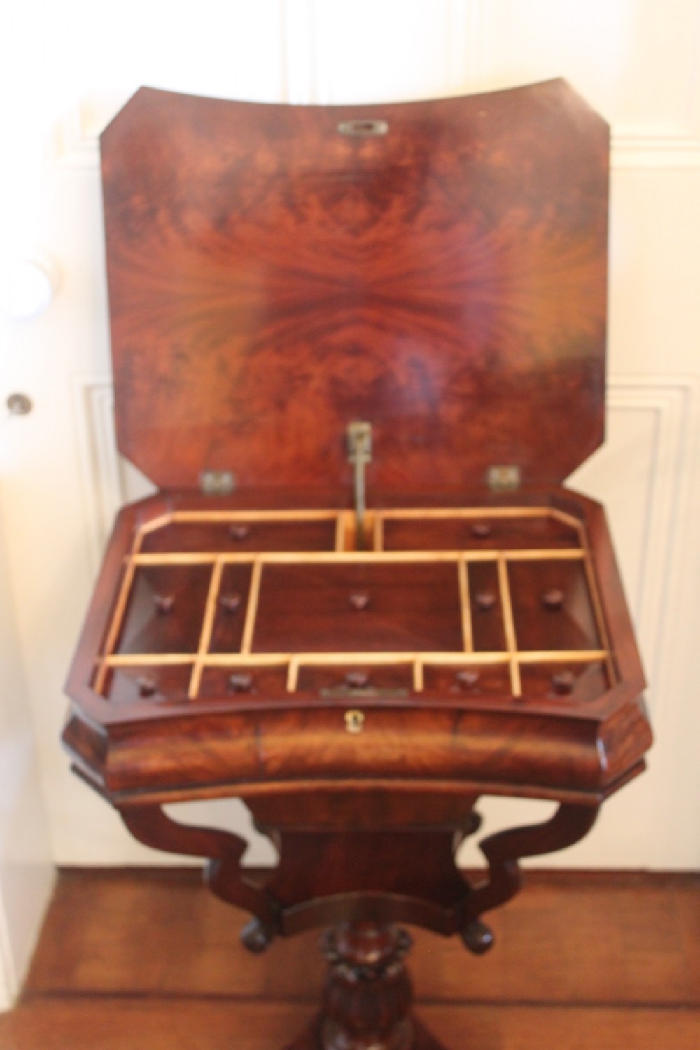 An early Victorian flame mahogany work table featuring a hinged top, carved central pedestal, triform base, and carved lion paw feet. View III