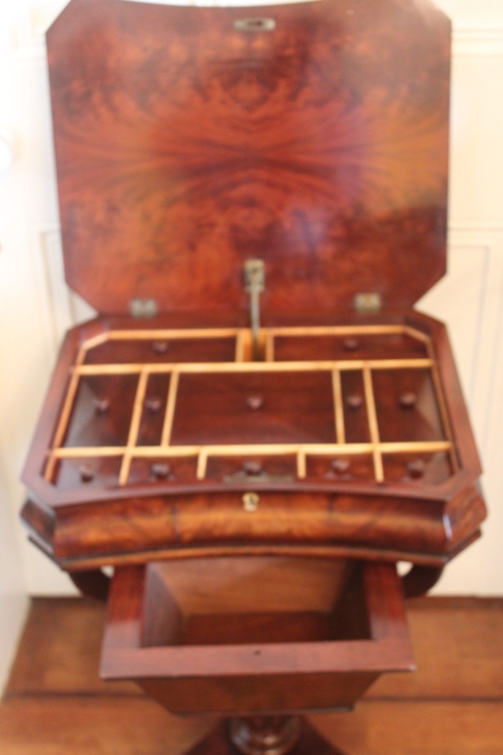 An early Victorian flame mahogany work table featuring a hinged top, carved central pedestal, triform base, and carved lion paw feet. View IV