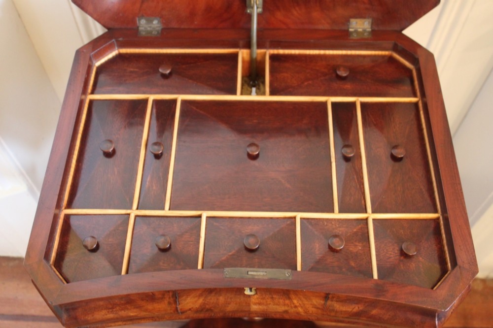 An early Victorian flame mahogany work table featuring a hinged top, carved central pedestal, triform base, and carved lion paw feet. View V