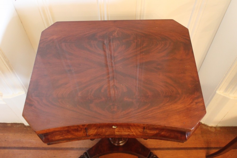 An early Victorian flame mahogany work table featuring a hinged top, carved central pedestal, triform base, and carved lion paw feet. View VII
