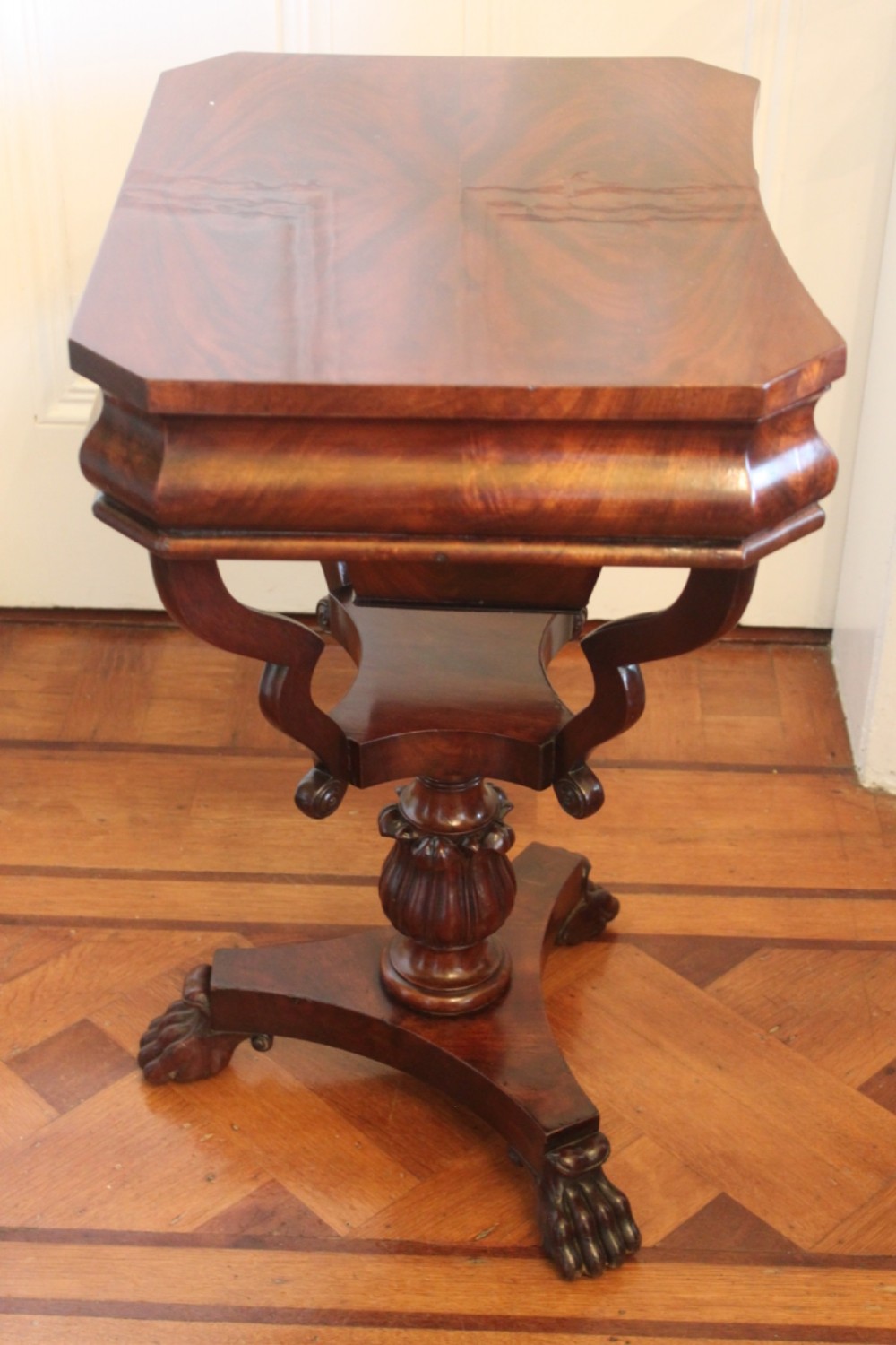 An early Victorian flame mahogany work table featuring a hinged top, carved central pedestal, triform base, and carved lion paw feet. View VIII