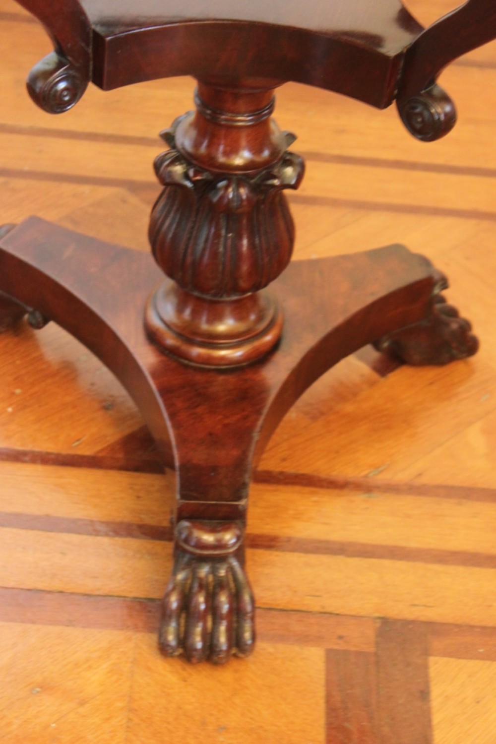 An early Victorian flame mahogany work table featuring a hinged top, carved central pedestal, triform base, and carved lion paw feet. View X