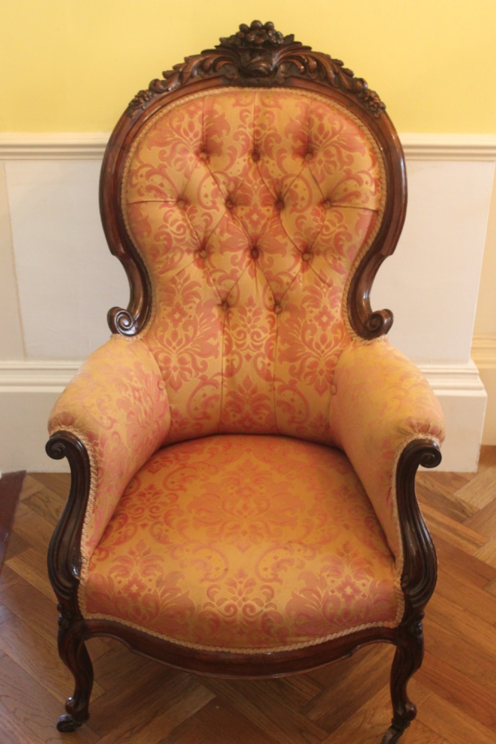 An early Victorian balloon-back gentlemans armchair with a carved dark mahogany frame, button-backed yellow damask upholstery, and cabriole legs.