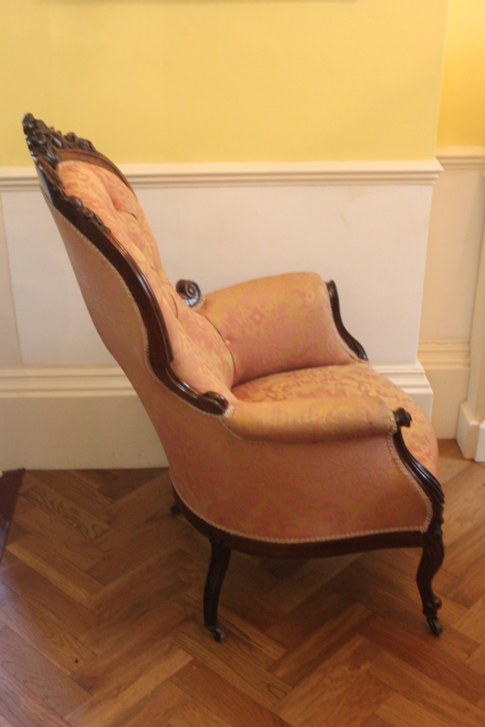 An early Victorian balloon-back gentlemans armchair with a carved dark mahogany frame, button-backed yellow damask upholstery, and cabriole legs. View IV