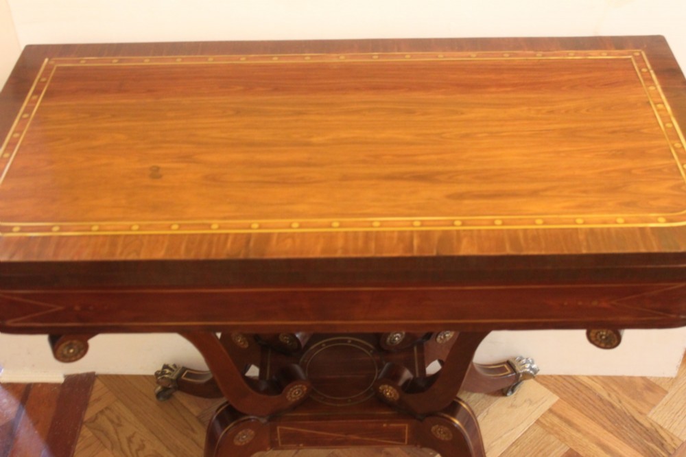 A Regency mahogany fold-over card table featuring geometric brass inlay, scroll supports, and brass paw feet on castors. View III
