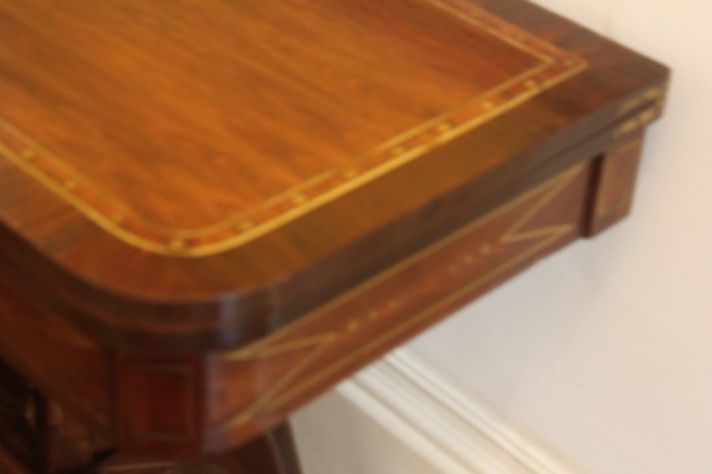 A Regency mahogany fold-over card table featuring geometric brass inlay, scroll supports, and brass paw feet on castors. View VI