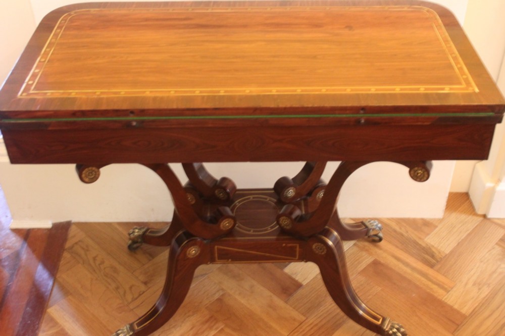 A Regency mahogany fold-over card table featuring geometric brass inlay, scroll supports, and brass paw feet on castors. View IX