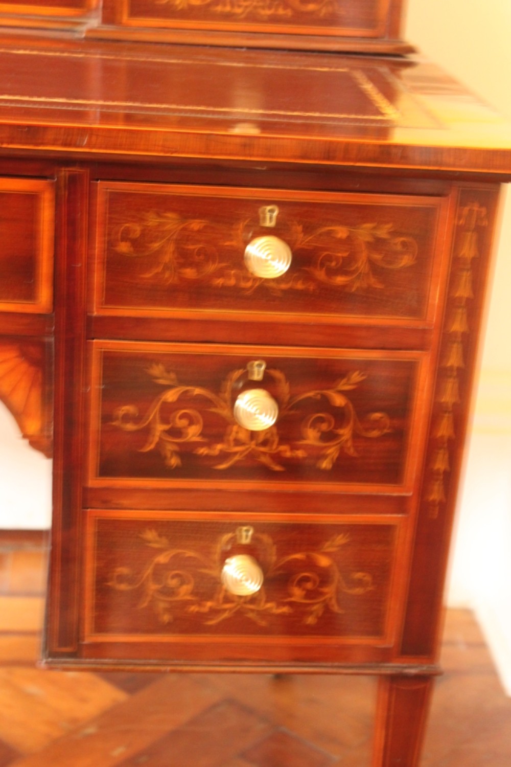 A Sheraton Revival mahogany writing desk featuring intricate marquetry inlays, a brown leather writing surface, a raised superstructure with small drawers, and square tapered legs. View II