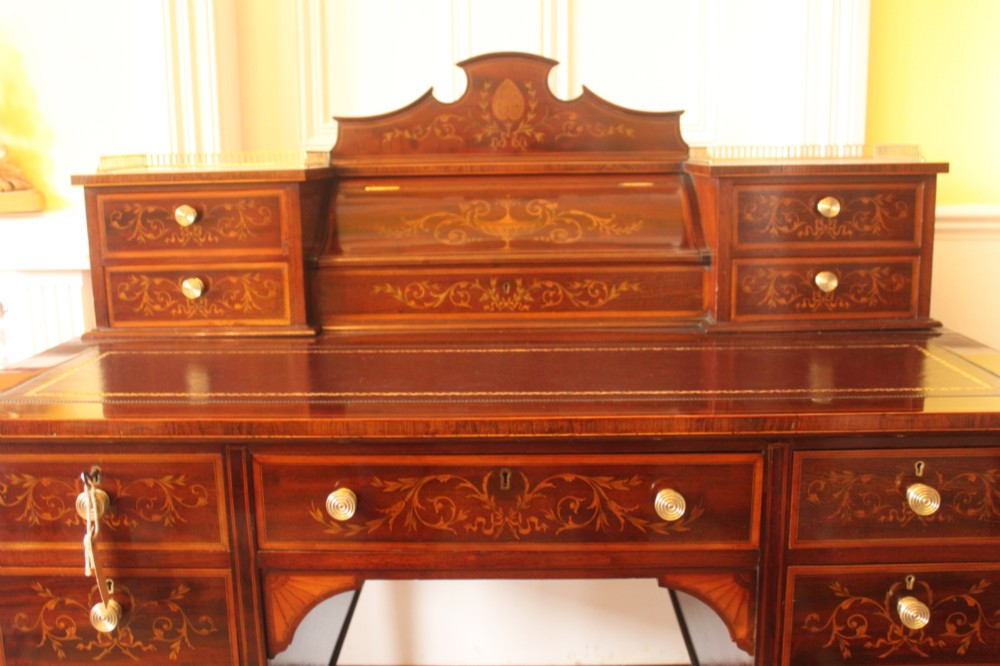 A Sheraton Revival mahogany writing desk featuring intricate marquetry inlays, a brown leather writing surface, a raised superstructure with small drawers, and square tapered legs. View IV