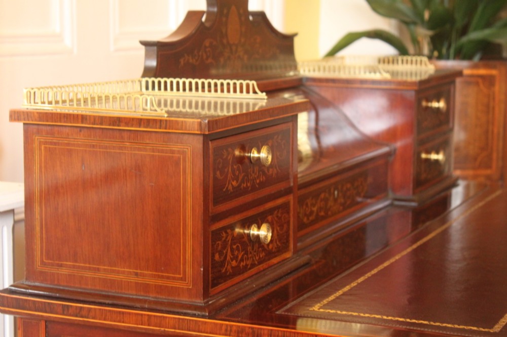 A Sheraton Revival mahogany writing desk featuring intricate marquetry inlays, a brown leather writing surface, a raised superstructure with small drawers, and square tapered legs. View XV