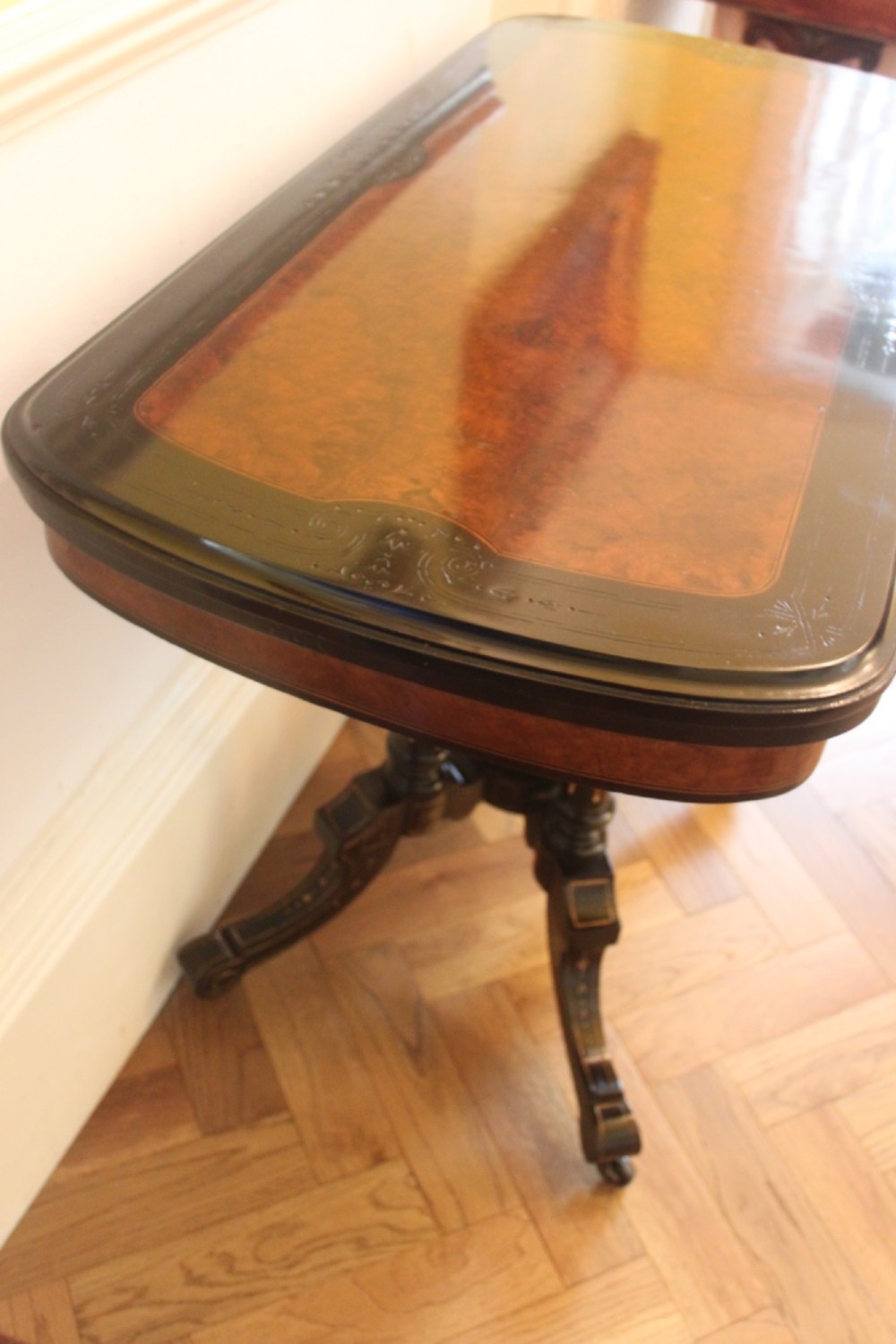 A Victorian foldover card table featuring a burr walnut top, ebonised border, double twin-column pedestal, and carved legs with castors. View V