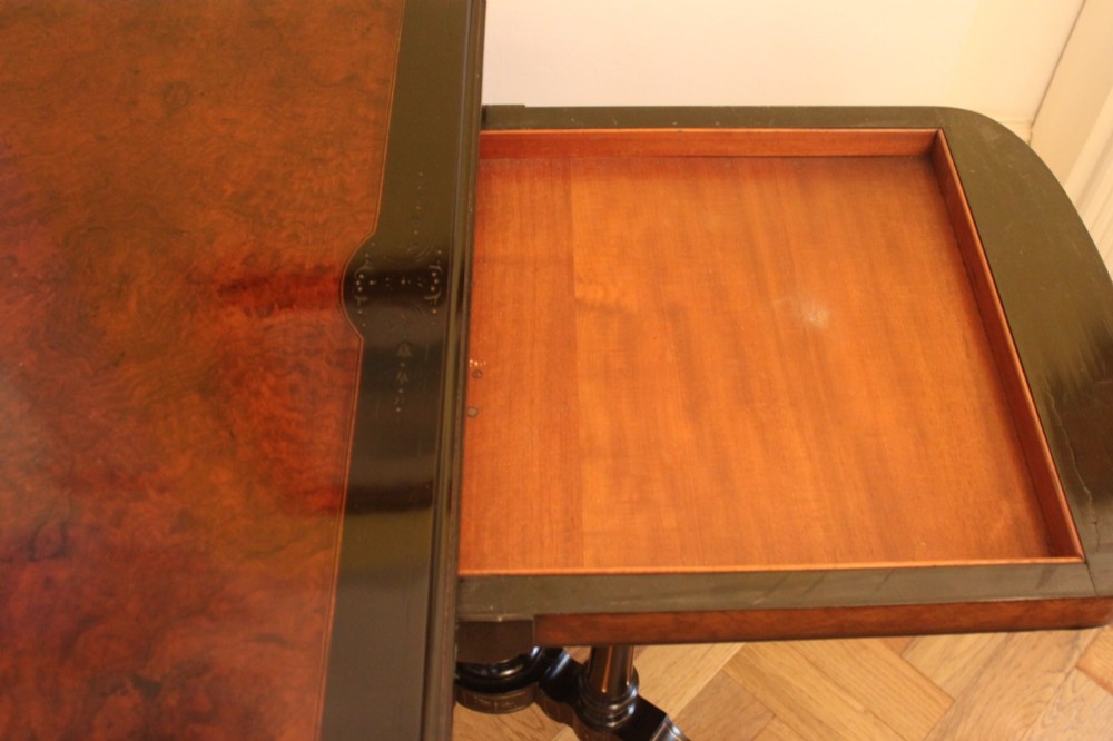 A Victorian foldover card table featuring a burr walnut top, ebonised border, double twin-column pedestal, and carved legs with castors. View IX