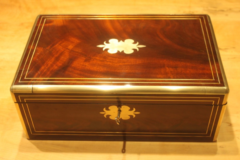 A rectangular curl grain mahogany writing slope box featuring fine brass stringing, brass bound corners, a central brass cartouche, and a keyhole escutcheon.