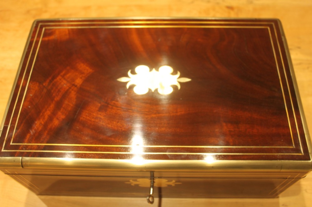 A rectangular curl grain mahogany writing slope box featuring fine brass stringing, brass bound corners, a central brass cartouche, and a keyhole escutcheon. View II