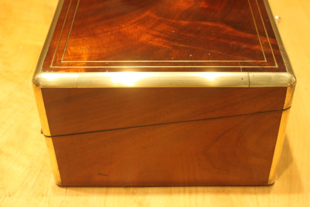 A rectangular curl grain mahogany writing slope box featuring fine brass stringing, brass bound corners, a central brass cartouche, and a keyhole escutcheon. View III