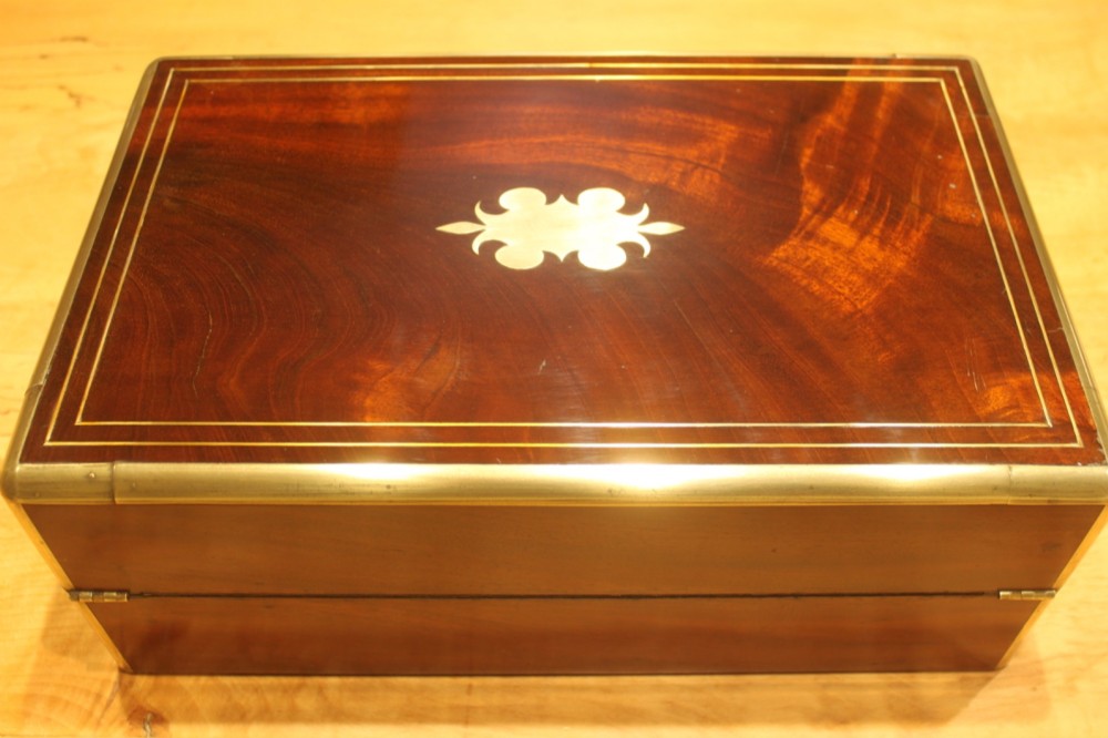 A rectangular curl grain mahogany writing slope box featuring fine brass stringing, brass bound corners, a central brass cartouche, and a keyhole escutcheon. View IV