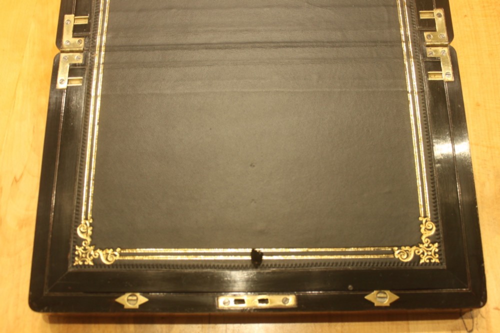 A rectangular curl grain mahogany writing slope box featuring fine brass stringing, brass bound corners, a central brass cartouche, and a keyhole escutcheon. View VII