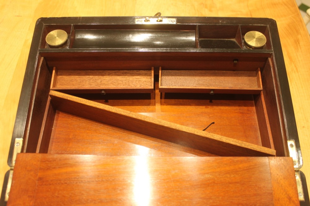 A rectangular curl grain mahogany writing slope box featuring fine brass stringing, brass bound corners, a central brass cartouche, and a keyhole escutcheon. View X