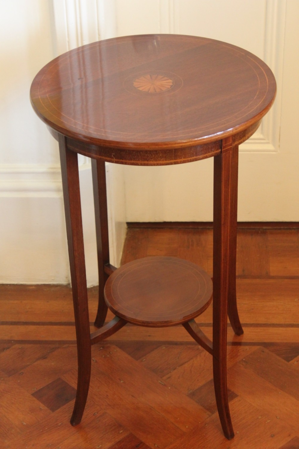A circular Edwardian mahogany occasional table featuring satinwood starburst inlay and a lower tier on slender splayed legs.