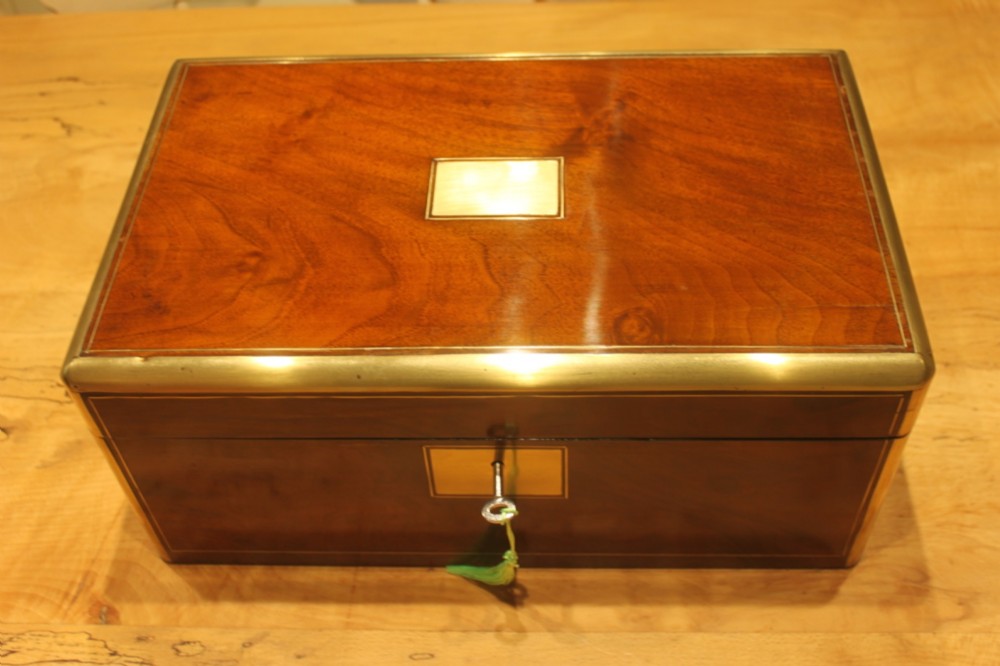 A closed rectangular Victorian walnut writing slope featuring brass binding, an inlaid brass central cartouche, and a keyhole escutcheon with a key.