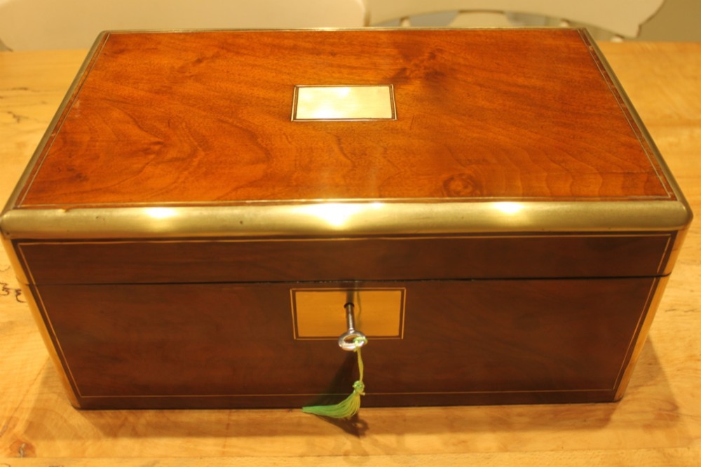 A closed rectangular Victorian walnut writing slope featuring brass binding, an inlaid brass central cartouche, and a keyhole escutcheon with a key. View II