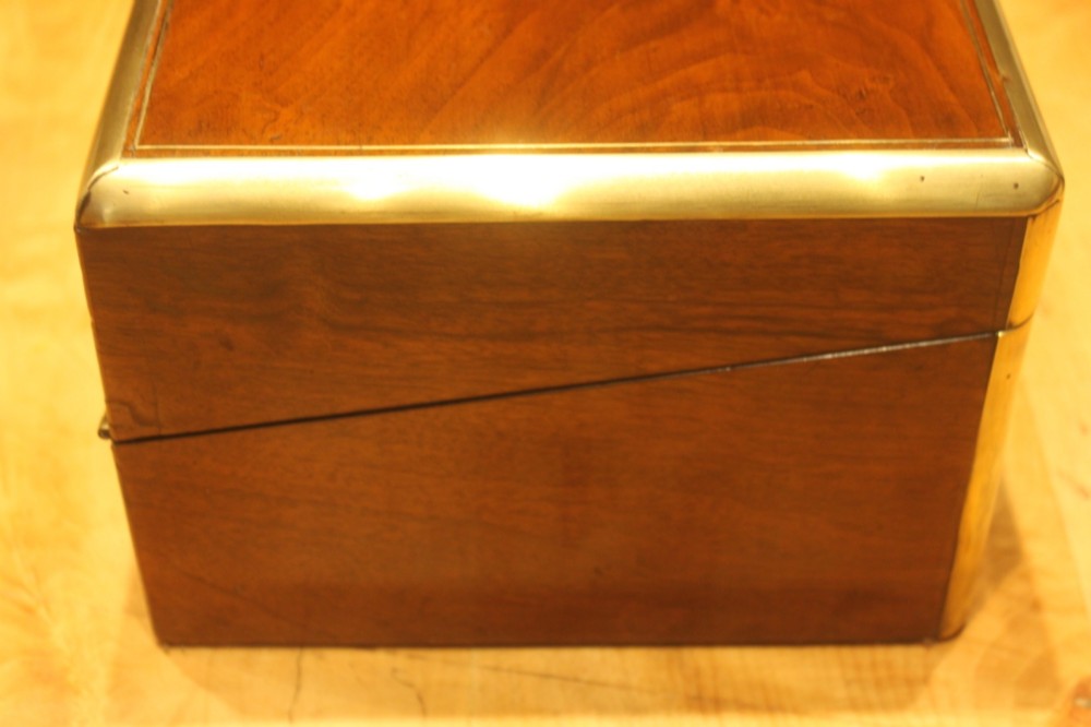 A closed rectangular Victorian walnut writing slope featuring brass binding, an inlaid brass central cartouche, and a keyhole escutcheon with a key. View III