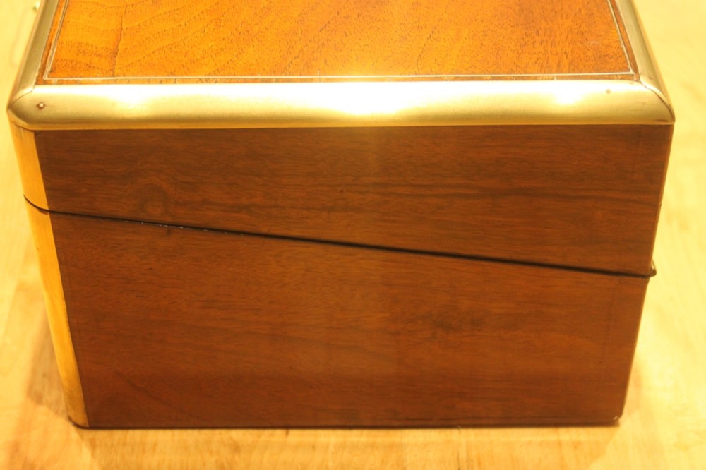 A closed rectangular Victorian walnut writing slope featuring brass binding, an inlaid brass central cartouche, and a keyhole escutcheon with a key. View V