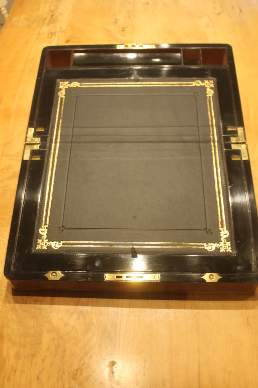 A closed rectangular Victorian walnut writing slope featuring brass binding, an inlaid brass central cartouche, and a keyhole escutcheon with a key. View VI