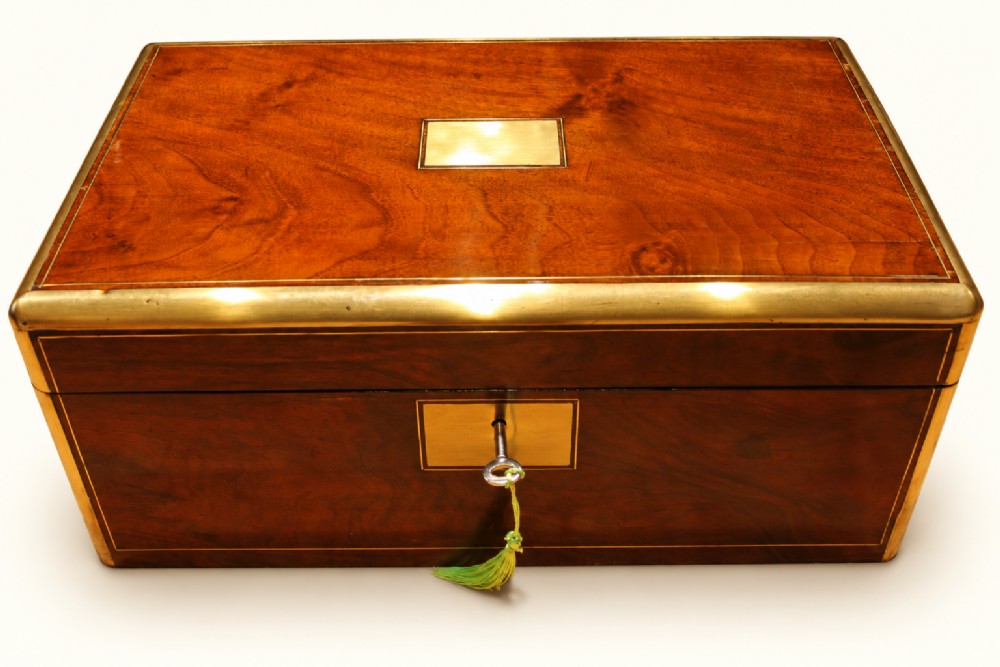 A rectangular Victorian walnut writing slope box featuring polished brass edge binding, a central brass inlaid plaque, and a key inserted into the front lock.