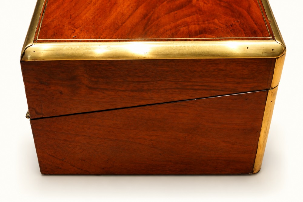 A rectangular Victorian walnut writing slope box featuring polished brass edge binding, a central brass inlaid plaque, and a key inserted into the front lock. View II