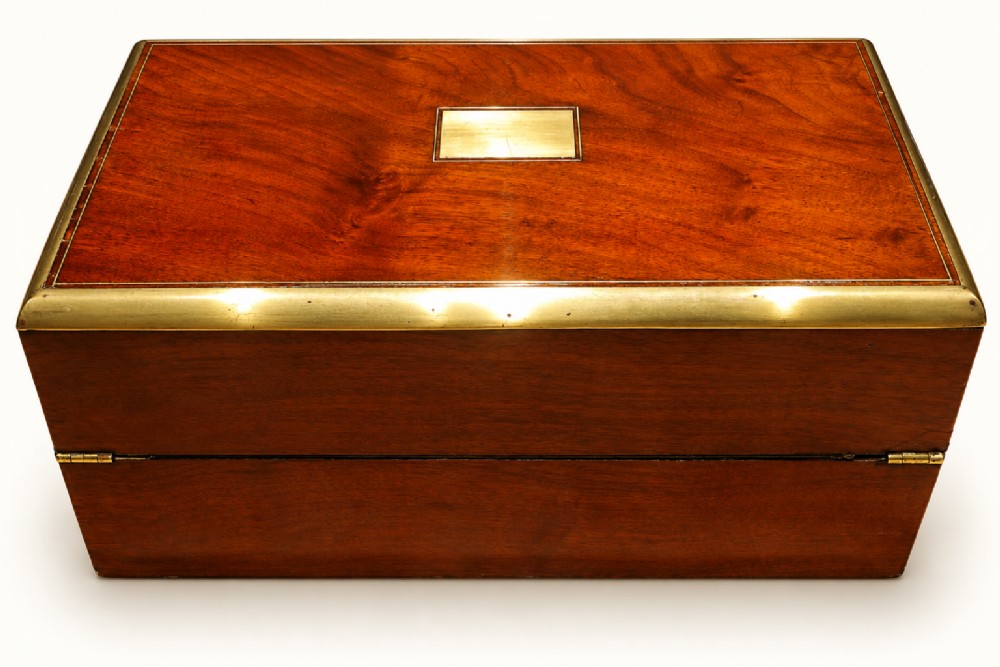 A rectangular Victorian walnut writing slope box featuring polished brass edge binding, a central brass inlaid plaque, and a key inserted into the front lock. View III