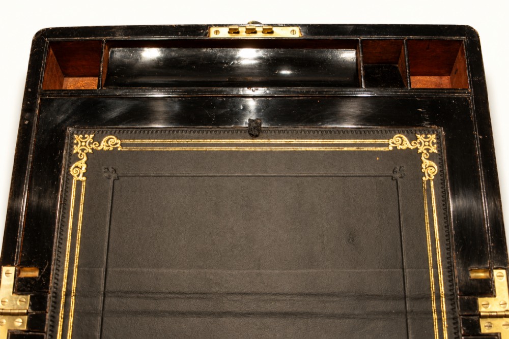 A rectangular Victorian walnut writing slope box featuring polished brass edge binding, a central brass inlaid plaque, and a key inserted into the front lock. View VII