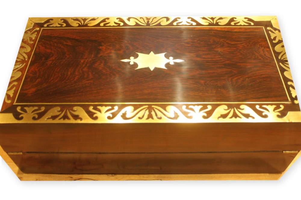 A closed rectangular dark rosewood writing slope box featuring detailed brass foliate inlay along the borders and a brass key inserted into the front lock. View III