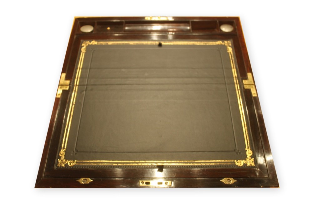 A closed rectangular dark rosewood writing slope box featuring detailed brass foliate inlay along the borders and a brass key inserted into the front lock. View V