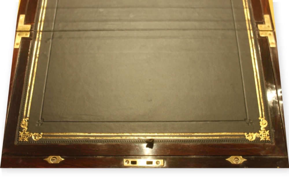 A closed rectangular dark rosewood writing slope box featuring detailed brass foliate inlay along the borders and a brass key inserted into the front lock. View VI