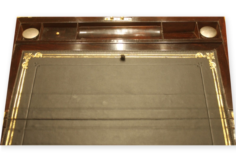 A closed rectangular dark rosewood writing slope box featuring detailed brass foliate inlay along the borders and a brass key inserted into the front lock. View VIII
