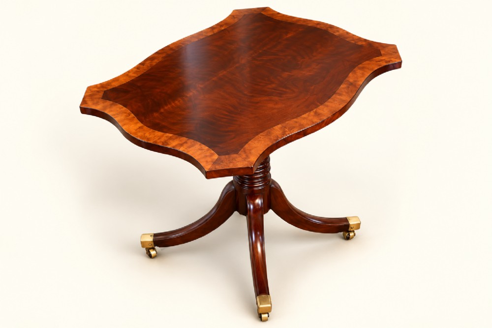 A 19th-century mahogany occasional table featuring a serpentine-shaped tilt top with decorative crossbanding, a turned pedestal base, and four splayed legs ending in brass toe caps. View VII
