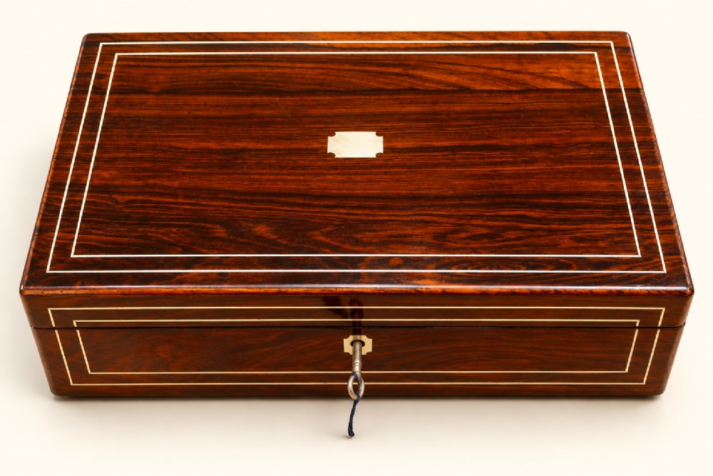 A rectangular dark rosewood wooden writing slope featuring double brass stringing inlay, a central brass cartouche, and an escutcheon with an inserted key.