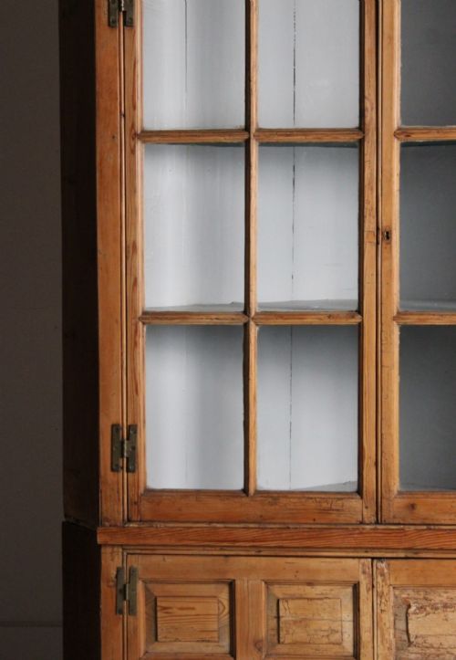 A tall freestanding pine corner cupboard featuring a glazed upper display section with multi-pane glass doors above a two-door lower cabinet with raised timber panels. View IV