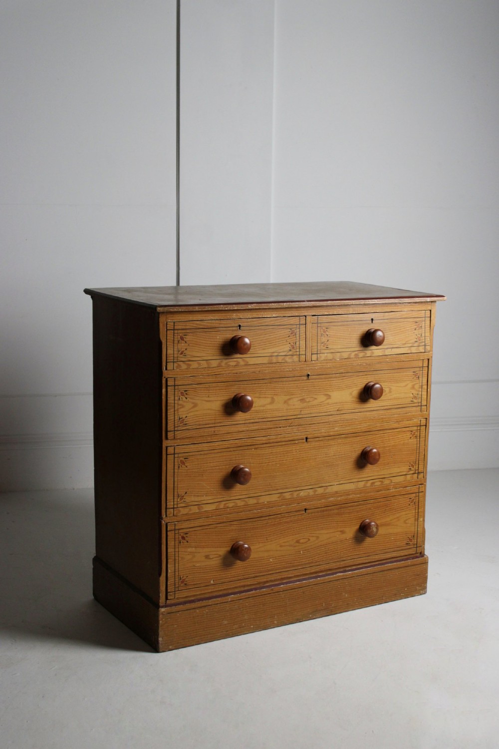 A 19th-century pine chest of drawers with a warm brown scumbled paint finish, featuring two short drawers over three long drawers with turned wooden knobs.