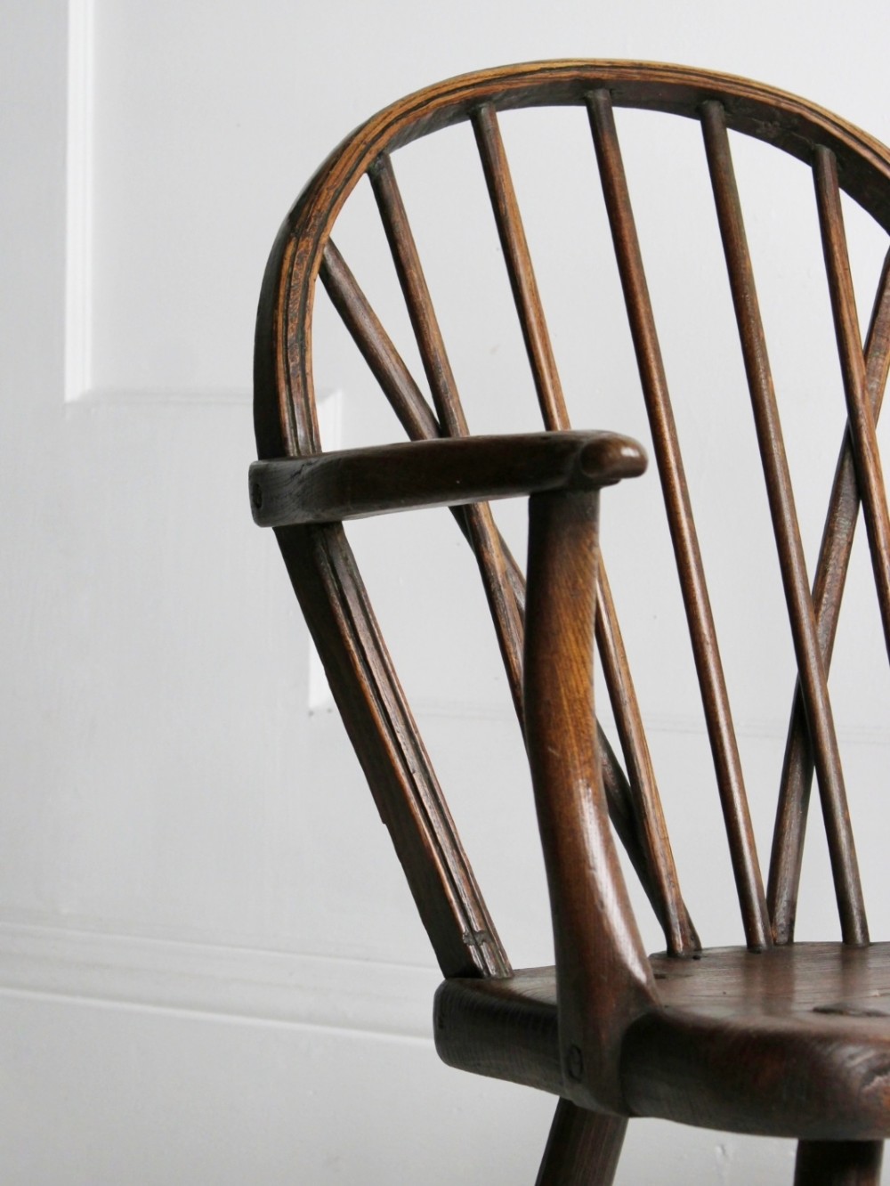 An 18th-century vernacular dark wooden armchair featuring a stick back design, curved armrests, a solid slab seat, and splayed legs. View V