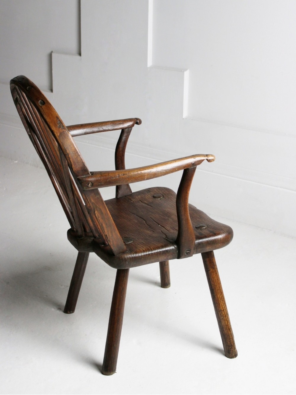 An 18th-century vernacular dark wooden armchair featuring a stick back design, curved armrests, a solid slab seat, and splayed legs. View VI
