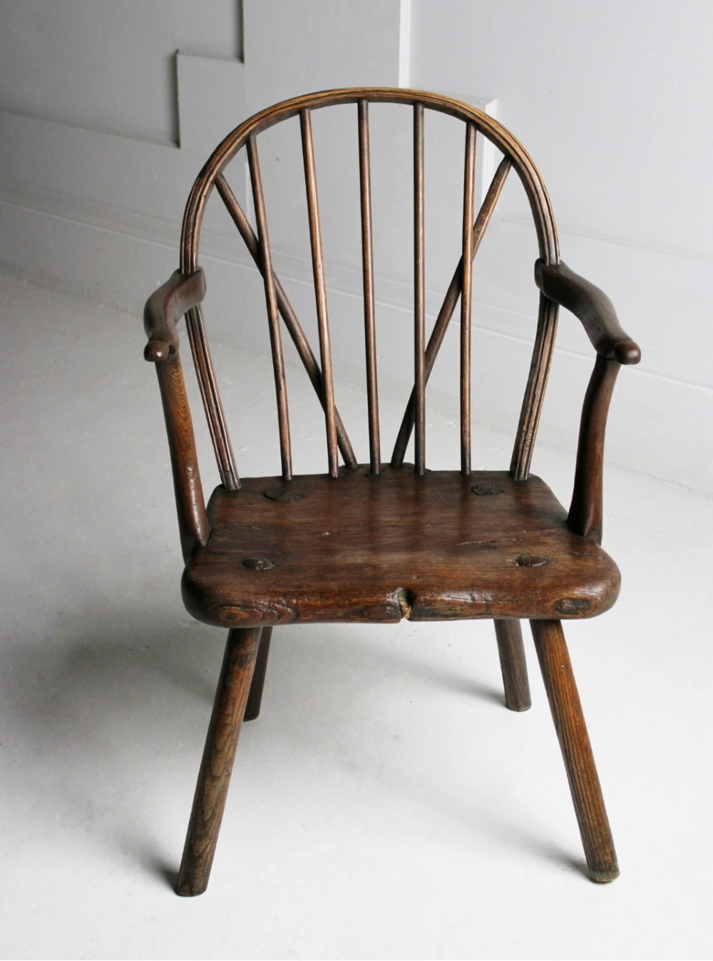 An 18th-century vernacular dark wooden armchair featuring a stick back design, curved armrests, a solid slab seat, and splayed legs. View VII