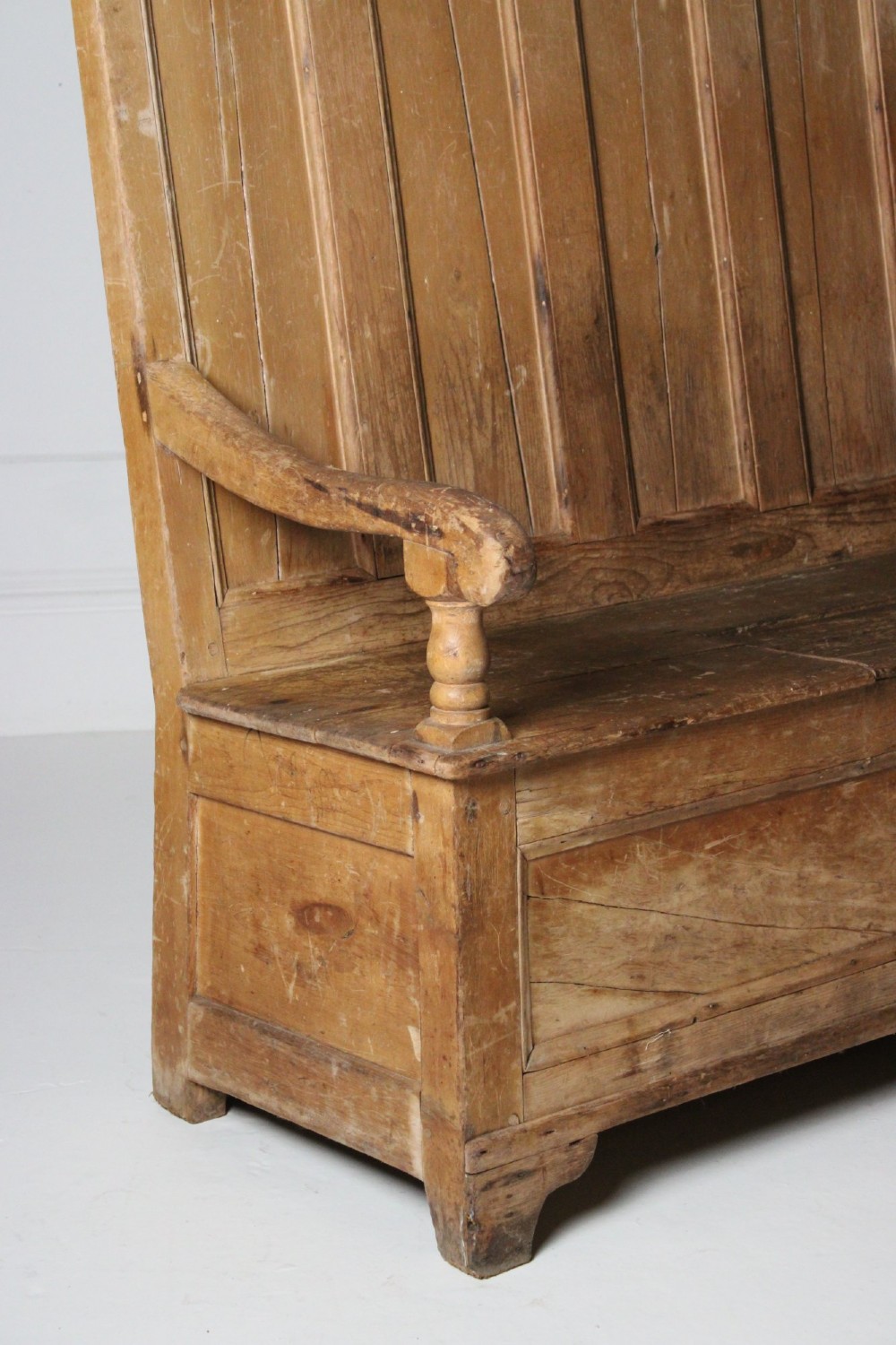 A 19th-century pine box settle featuring a high panelled back rest, curved armrests on turned supports, and an enclosed base incorporating a seat storage compartment. View II