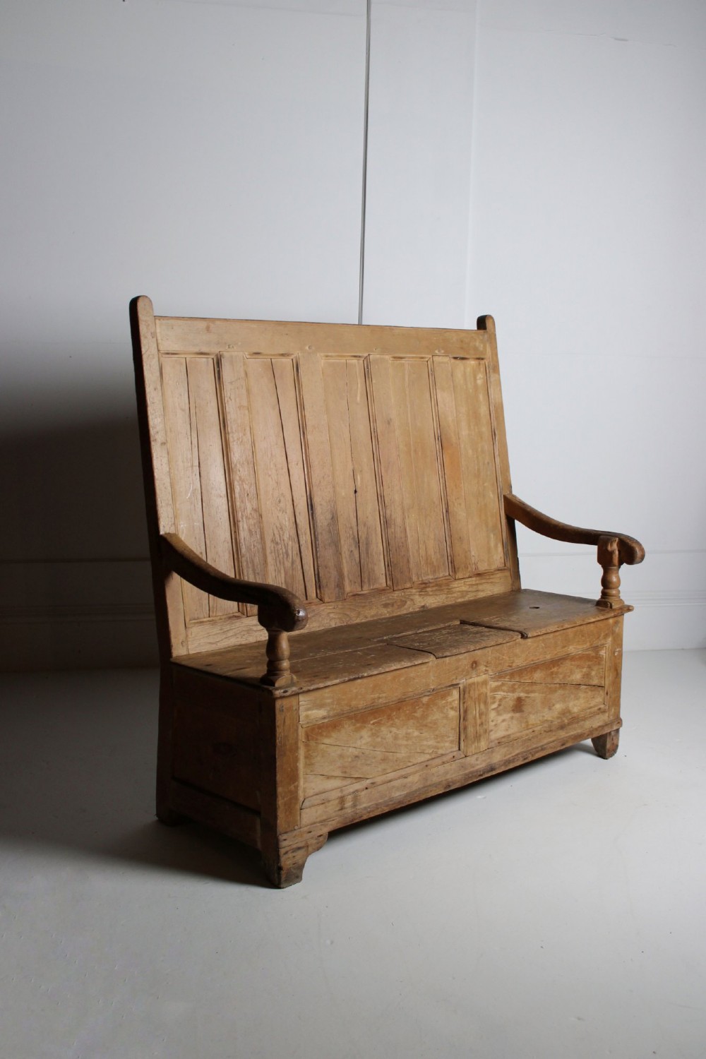A 19th-century pine box settle featuring a high panelled back rest, curved armrests on turned supports, and an enclosed base incorporating a seat storage compartment. View III