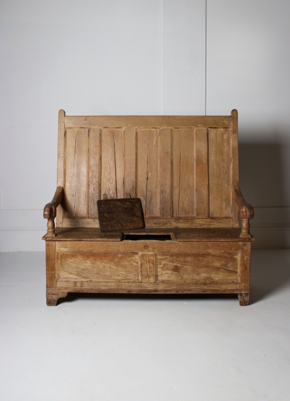 A 19th-century pine box settle featuring a high panelled back rest, curved armrests on turned supports, and an enclosed base incorporating a seat storage compartment. View IV
