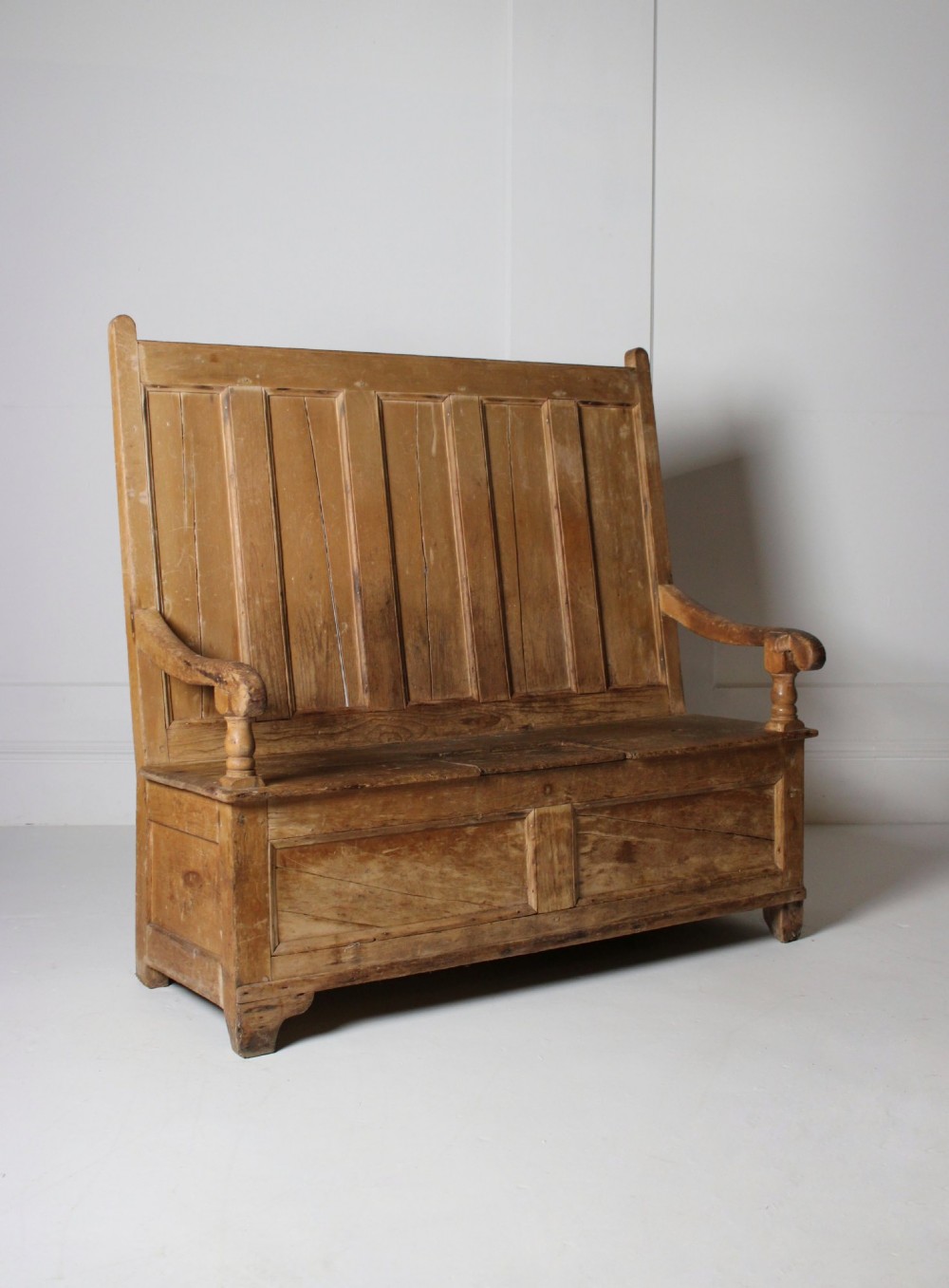 A 19th-century pine box settle featuring a high panelled back rest, curved armrests on turned supports, and an enclosed base incorporating a seat storage compartment.