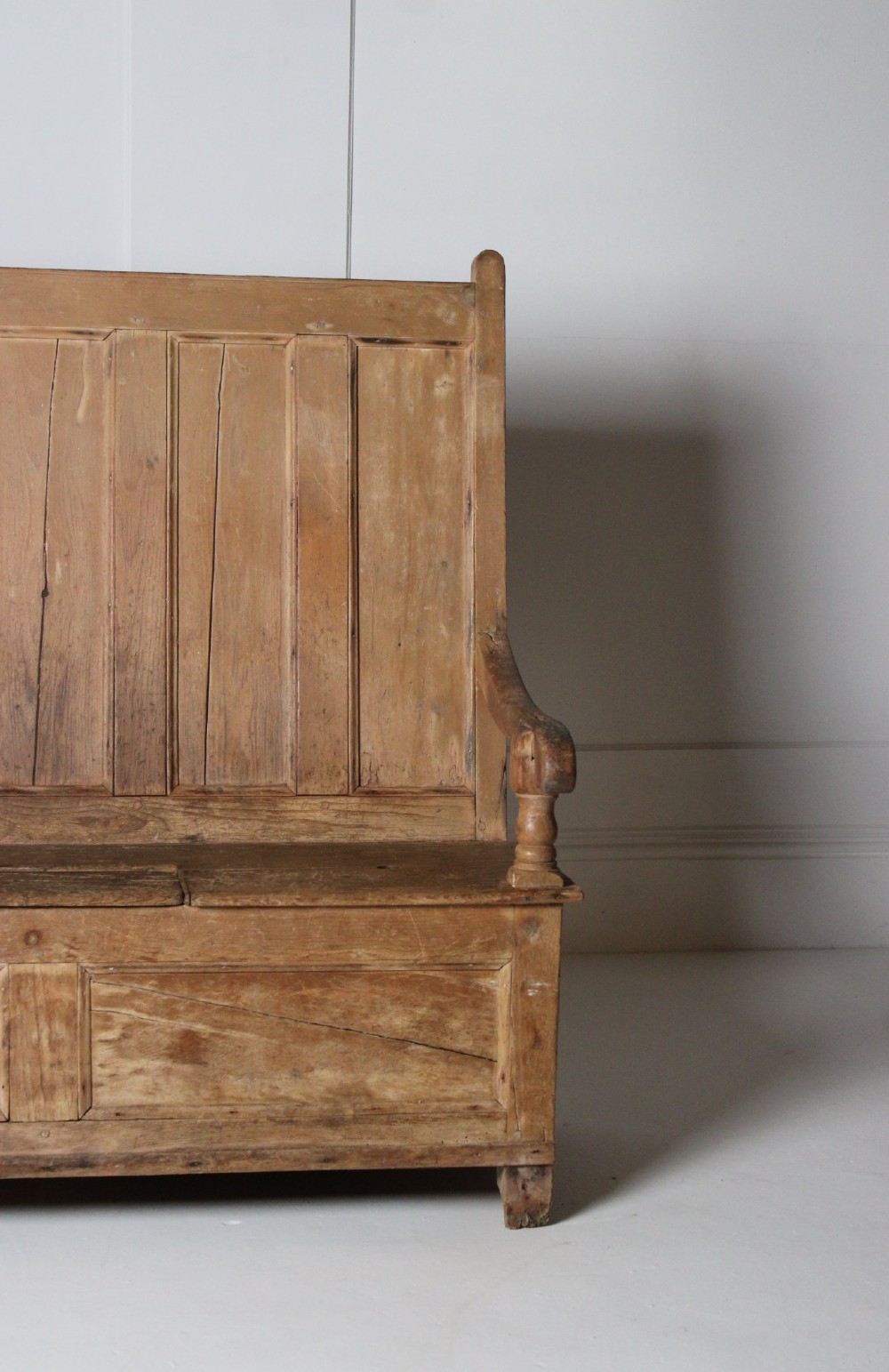 A 19th-century pine box settle featuring a high panelled back rest, curved armrests on turned supports, and an enclosed base incorporating a seat storage compartment. View V